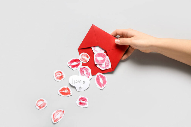 Женская рука с красным конвертом, бумажные следы поцелуев помады и текст, который я люблю тебя на сером фоне, крупным планом. Празднование Дня Святого Валентина - Фото, изображение