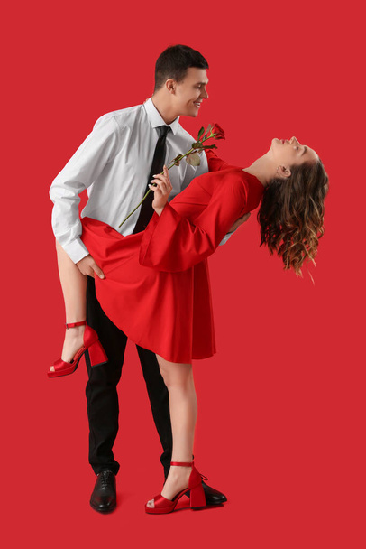 Happy young couple with rose flower dancing on red background. Valentine's day celebration - Photo, Image