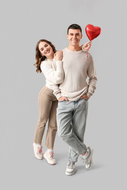 Happy young couple with heart-shaped air balloon on pink background. Valentine's day celebration - Photo, Image