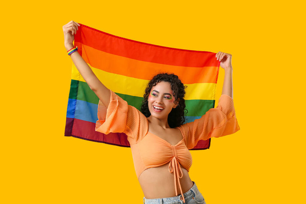 Junge afroamerikanische Frau mit Regenbogenfahne auf gelbem Hintergrund. Homosexualität - Foto, Bild