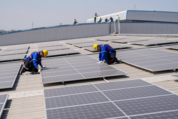 Profesjonalni inżynierowie sprawdzają dach słoneczny na dachu fabryki w świetle słonecznym. Inżynierowie wykonujący prace serwisowe w zakresie energii elektrycznej odnawialnej - Zdjęcie, obraz