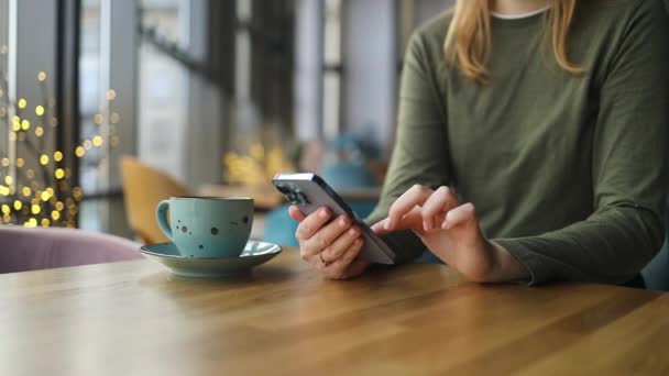 Crop view of female person holding smartphone and scrolling mobile phone while sitting at table with coffee at coffee shop cafe. Werknemers nemen contact op met marketing business, technologie. Hoge kwaliteit FullHD - Video