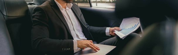 Уверенность бизнесмен сидит на заднем сиденье автомобиля и работает с документами и использовать ноутбук - Фото, изображение