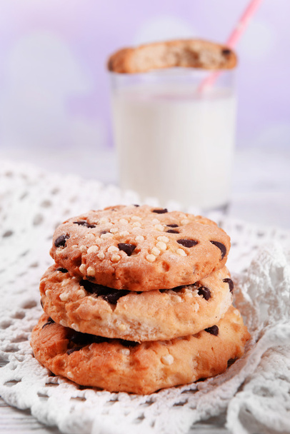 Biscotti saporiti e vetro di latte su tavolo di legno di colore, su sfondo lucente
 - Foto, immagini