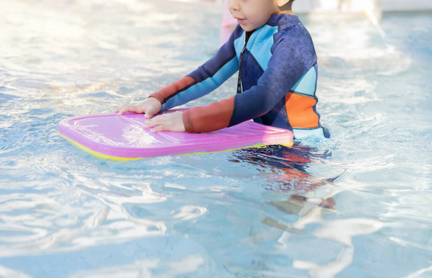 Lonely child warm up with swimming kickboard before practicing to swim in the blue swimming pools. - Photo, Image