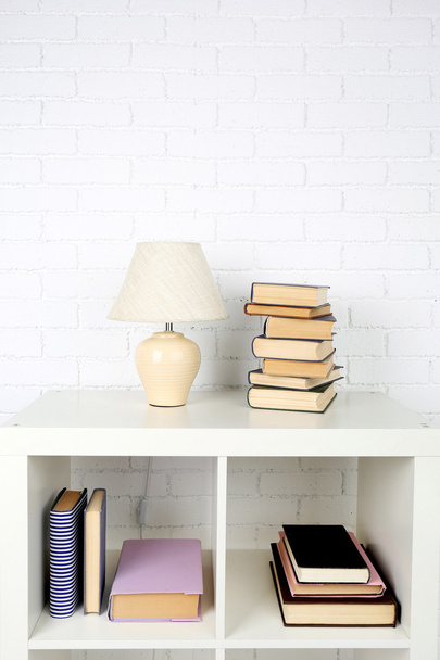 Wooden shelf with books and lamp on brick wall background - Fotó, kép
