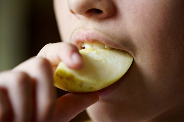 Closeup of crop unrecognizable young girl biting fresh juicy apple piece at home - Photo, Image