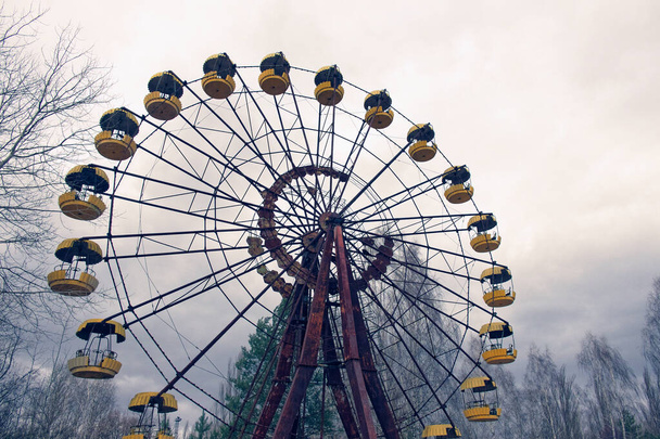 Старое колесо обозрения с желтыми гондолами, окруженное деревьями. - Фото, изображение
