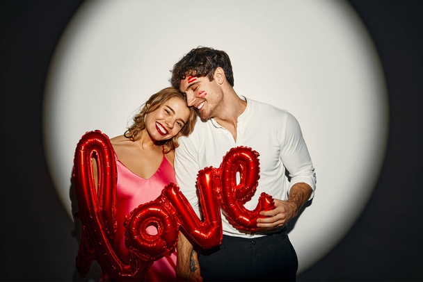 Szczęśliwych Walentynek. Para zakochanych trzymająca balon z napisem miłość na białym tle w świetle reflektorów. - Zdjęcie, obraz