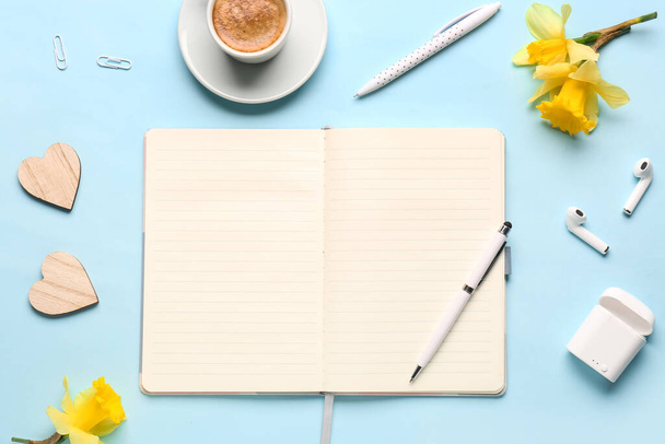 Samenstelling met notitieboekje, kop koffie, oortjes en mooie narcissen bloemen op blauwe achtergrond - Foto, afbeelding