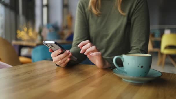 Vrouwelijke handen die smartphone vasthouden, drinken en genieten van koffie op houten tafel in café, close-up. Hoge kwaliteit FullHD beeldmateriaal - Video