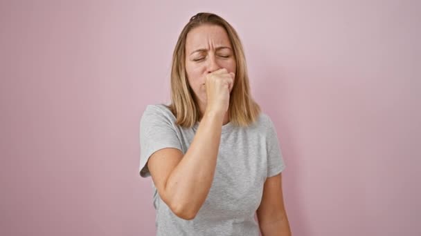 Jonge blonde vrouw hoesten over geïsoleerde roze achtergrond, belichaamt de expressieve strijd van griep-achtige symptomen in deze levendige tijden - Video