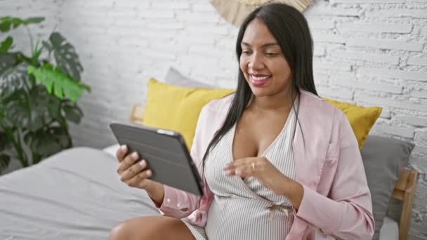 Genç hamile bir kadın rahat pijamalarıyla internetten sohbet ediyor. Yatak odasında uzanırken karnını okşuyor. - Video, Çekim