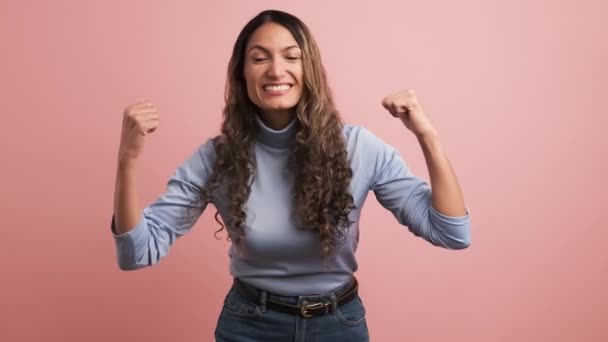Latin bir kadının yumruklarıyla kutlama yaparken el kol hareketi yaptığı pembe arkaplanlı bir video. - Video, Çekim