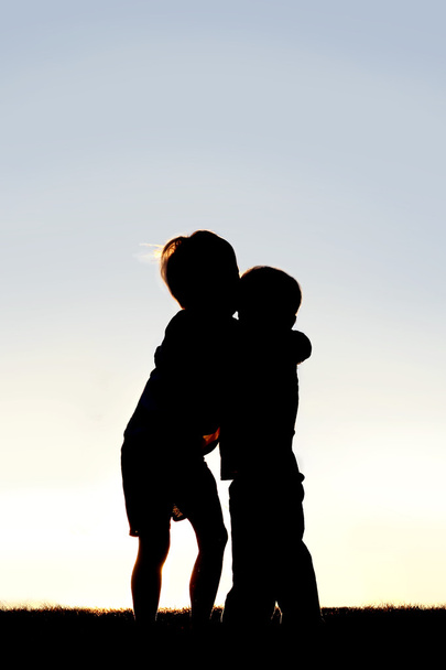 Kahden pienen lapsen siluetti halaamassa auringonlaskun aikaan
 - Valokuva, kuva
