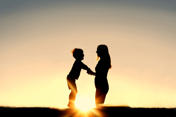 Siluetti äiti ja pieni lapsi tilalla kädet auringonlaskun aikaan
 - Valokuva, kuva
