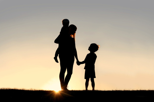 Silhouet van moeder en jonge kinderen hand in hand bij zonsondergang - Foto, afbeelding