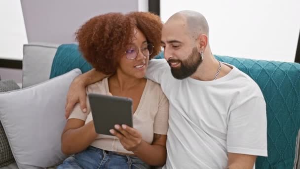 Hermosa pareja sonriente sentados juntos en casa, disfrutando con confianza en línea vinculación sobre touchpad, irradiando alegría en su encantadora relación de sala de estar interior - Metraje, vídeo