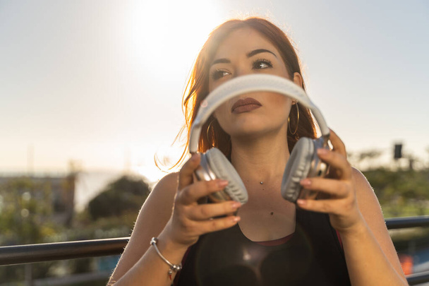 Une jeune femme tient son casque en prévision d'une séance de musique relaxante lors d'un coucher de soleil serein. - Photo, image
