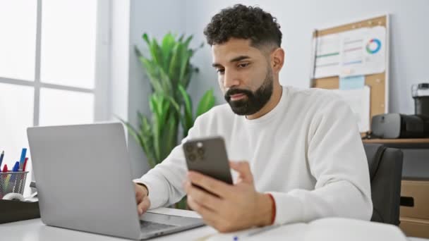 Um homem adulto hispânico profissional focado em seu smartphone em um ambiente de escritório moderno, combinando elementos de tecnologia, trabalho e concentração. - Filmagem, Vídeo