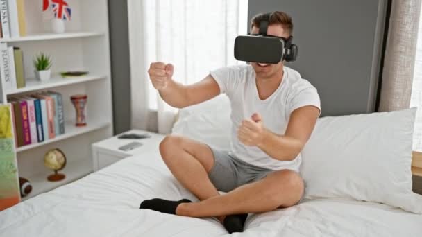 VR kulaklıklı genç adam modern bir yatak odasında heyecanla el kol hareketi yapıyor. - Video, Çekim