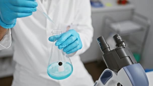 Científico en bata de laboratorio realizando experimento con líquido azul en frasco en banco de laboratorio. - Imágenes, Vídeo