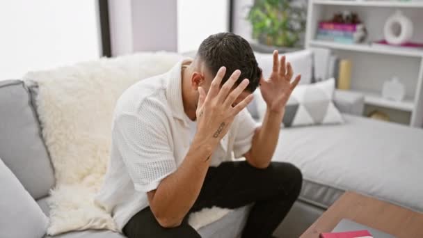 Wanhopige jonge Arabier man thuis, navigeren stress, migraine, lijden en pijn tijdens het zitten op een bank, met de hand cradling hoofd - Video