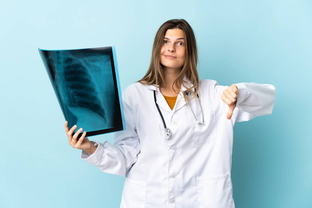 Jovem médica segurando radiografia sobre fundo isolado mostrando polegar para baixo com expressão negativa - Foto, Imagem