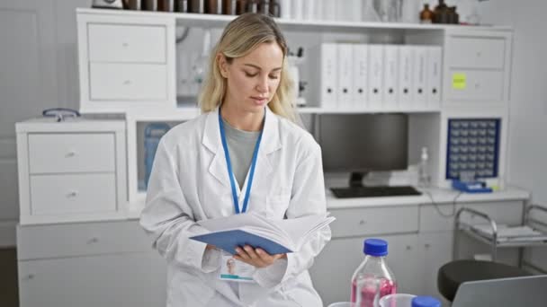 Une femme caucasienne concentrée en blouse lit un manuel à l'intérieur d'un laboratoire bien équipé. - Séquence, vidéo