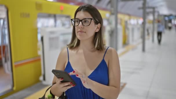 Vidám, szemüveges spanyol nő elmerül egy mosolygó telefonos utazásban, elnyeli a város rezgéseit, miközben a ginza metróállomás peronján áll, és az utazóvasútra vár.. - Felvétel, videó