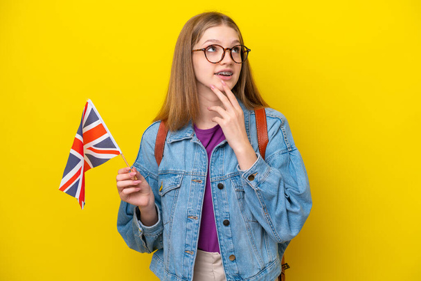 Teenager russische Mädchen mit einer Flagge des Vereinigten Königreichs isoliert auf gelbem Hintergrund blickt auf, während lächelnd - Foto, Bild
