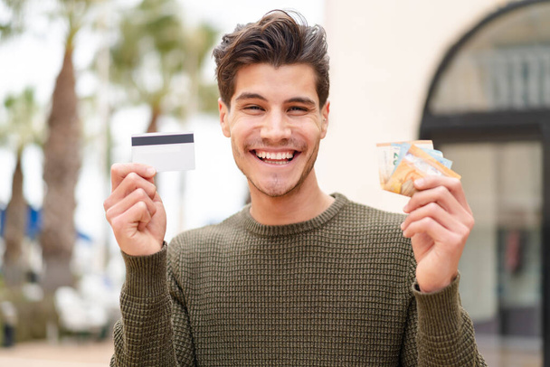 Jeune homme caucasien à l'extérieur prenant beaucoup d'argent avec expression heureuse - Photo, image