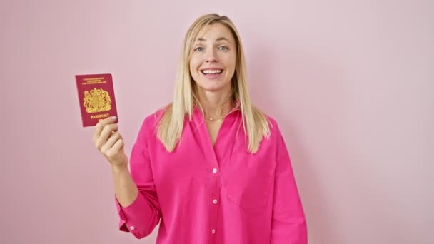 Joyeux jeune femme blonde, les bras levés dans le triomphe victorieux, poutres avec fierté tenant passeport Irlande du Nord sur fond rose isolé. célébration de la réussite. - Séquence, vidéo