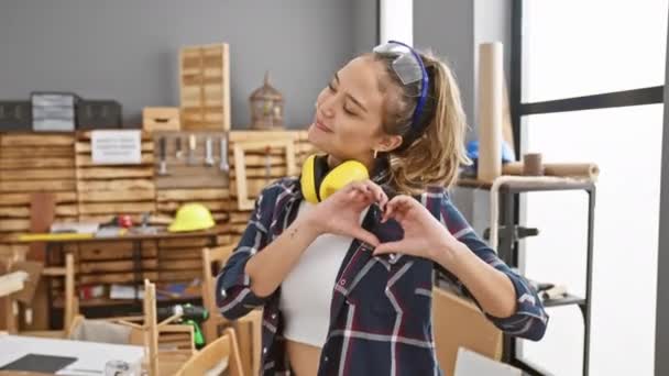 Συγκινητική θέα μιας νεαρής, όμορφης Ισπανίδας που κάνει έρωτα με τα χέρια της, χαμογελώντας στο εργαστήρι ξυλουργικής της, φορώντας ακουστικά και γυαλιά ασφαλείας - Πλάνα, βίντεο