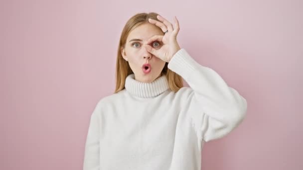 Geschokt mooi blond meisje kijken door ok-gebaar vingers, verrast uitdrukking over geïsoleerde roze achtergrond - Video