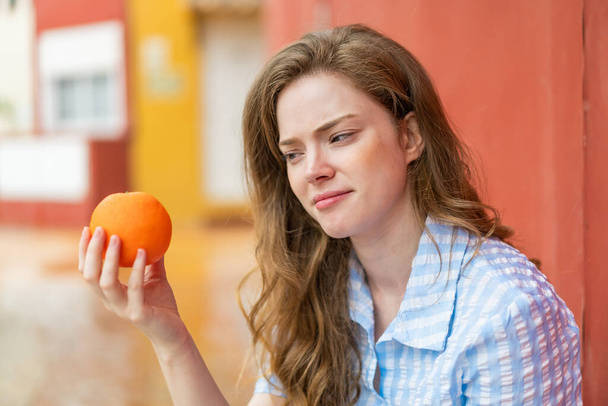 Joven pelirroja al aire libre sosteniendo una naranja - Foto, imagen