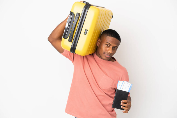 Young latin man isolated on white background in vacation with suitcase and passport - Photo, Image