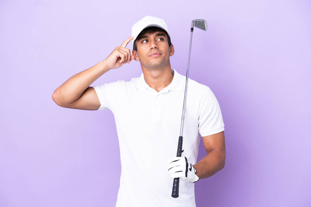 Joven hombre caucásico aislado sobre fondo púrpura jugando golf y y teniendo dudas confundir la expresión de la cara - Foto, imagen