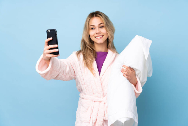 Mavi arka planda izole edilmiş pijamalı genç Rus kız selfie çekiyor. - Fotoğraf, Görsel