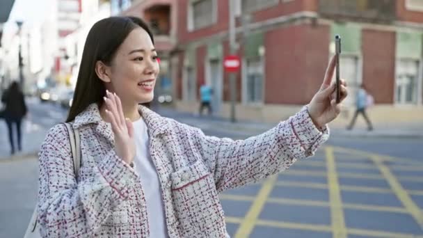 Mujer asiática joven toma selfie en la esquina de la calle de la ciudad, sonriendo, casual, sosteniendo el teléfono inteligente, de moda, al aire libre. - Metraje, vídeo