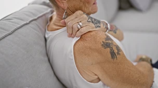 Starsza siwowłosa kobieta w agonii, siedząca na kanapie w salonie, zmagająca się z piekącym bólem pleców w domu - Materiał filmowy, wideo