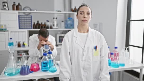 Deux scientifiques déterminés, un homme et une femme, travaillent ensemble dans un laboratoire, dépeignant une concentration sérieuse avec des bras croisés geste - Séquence, vidéo