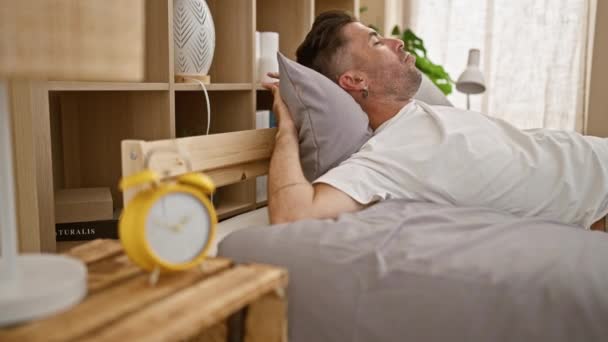 Kimerült fiatal spanyol férfi próbál sikertelenül sodródni egy hangulatos alvás, miközben feküdt az ágyban, takaró és párna ferdén, egy kényelmesen pihentető hálószoba belső otthon - Felvétel, videó