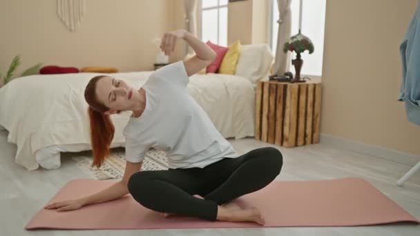 Спокойная рыжая женщина практикует йогу в спальне, воплощая спокойствие и равновесие в мирной домашней обстановке. - Кадры, видео
