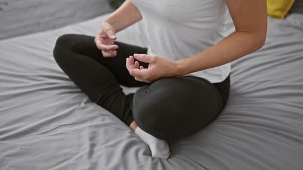 Obudzona kobieta, w odzieży sportowej, znajduje spokojną równowagę siedząc na łóżku, ręce opanowane w medytacyjnym ćwiczeniu jogi. przywołuje relaks i koncentrację w zaciszu jej przytulnej sypialni. - Materiał filmowy, wideo