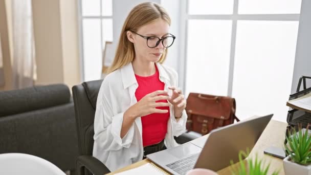 Mujer joven enfocada que trabaja en una computadora portátil en la oficina moderna brillante, mostrando profesionalismo y concentración. - Metraje, vídeo