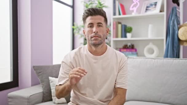 Knappe jonge Spaanse man die met de hand 'stop' zegt in zijn uitnodigende, huiselijke woonkamer - Video