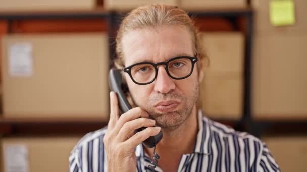 Un uomo serio con gli occhiali in camicia a righe parla al telefono in un magazzino. - Filmati, video
