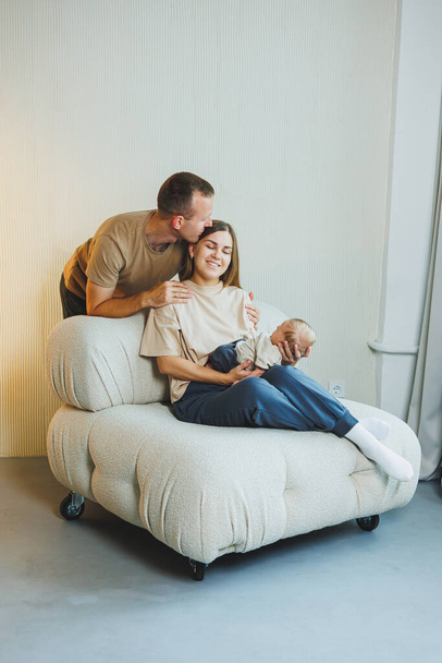 Nuoret onnelliset vanhemmat, joilla on vastasyntynyt vauva sylissään kotona sohvalla. Äiti ja isä, joilla on vastasyntynyt vauva valkoisella taustalla - Valokuva, kuva