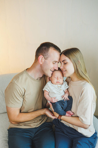 Μια νεαρή οικογένεια με ένα νεογέννητο μωρό. Ευτυχισμένοι γονείς που φιλούν το παιδί τους. Γονείς και ένα χαμογελαστό παιδί στην αγκαλιά τους - Φωτογραφία, εικόνα